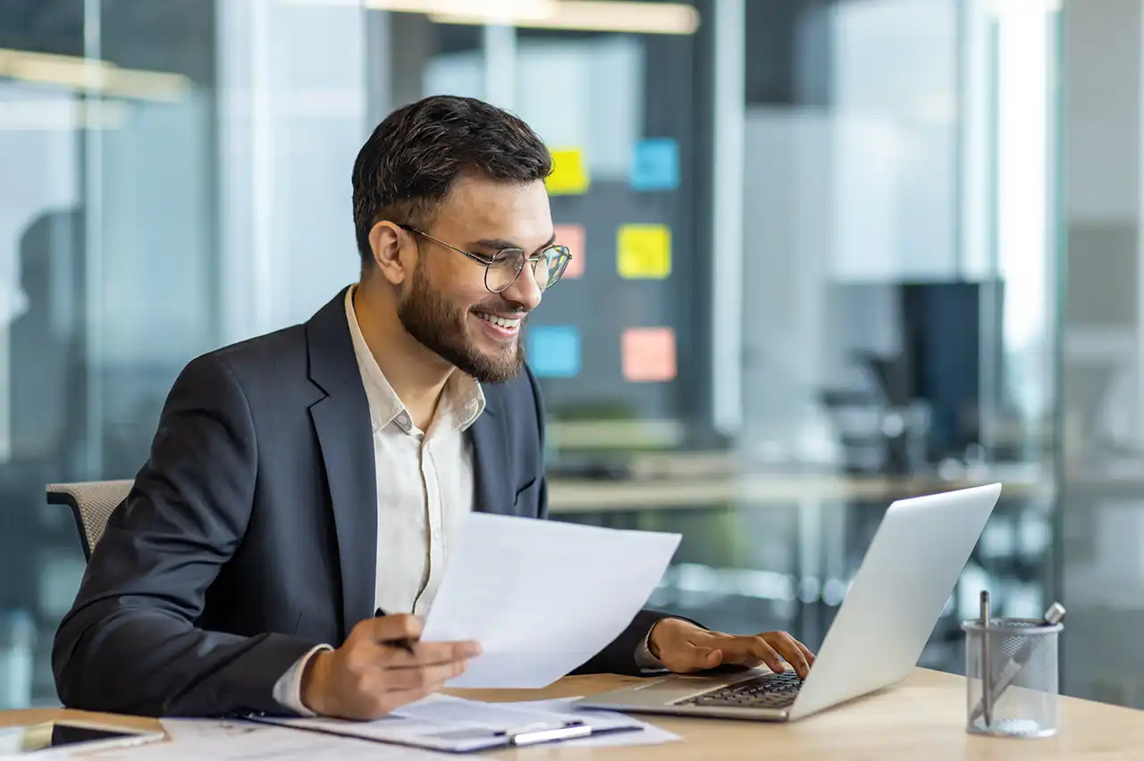 Business professional reviewing energy contract and utility billing documents at a laptop