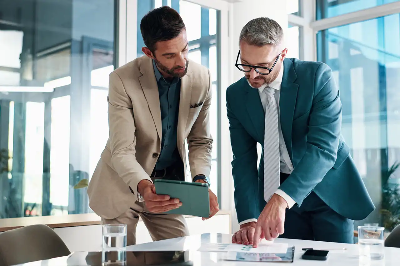 Connecting Facility Knowledge with Electric Billing Review Two business professionals reviewing printed documents and a tablet at an office table